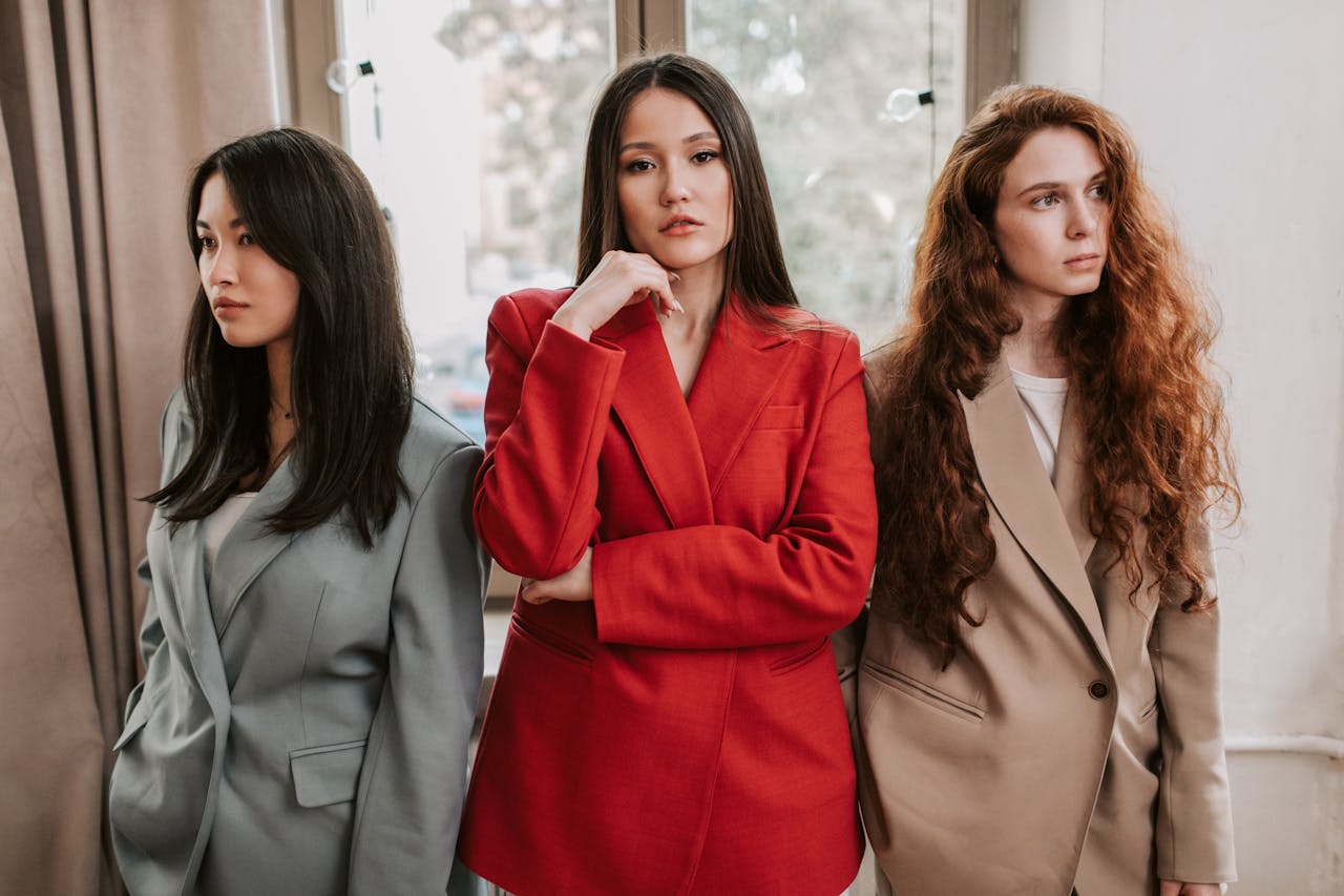 hero-img Three women in blazers posing with confidence, exuding modern fashion and style indoors.